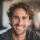 Homme souriant avec cheveux bouclés, en intérieur lumineux.